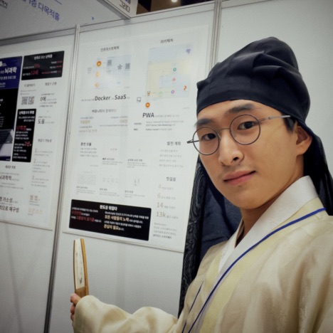 SuhJae wearing a yellow Hanbok (도포), presenting his project "BlueScript" poster at the Korea Creative Festival.